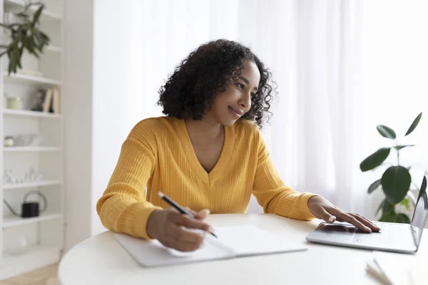Mujer negra usando laptop, trabajando o estudiando en línea, tomando notas durante videoconferencia o webinar en casa —  Fotos de Stock