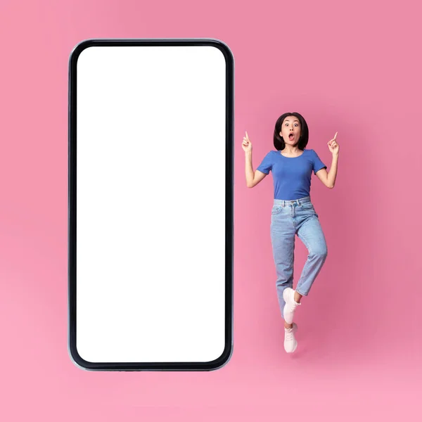 令人惊讶的亚洲女士在巨大的手机屏幕旁跳跃，粉色背景 — 图库照片