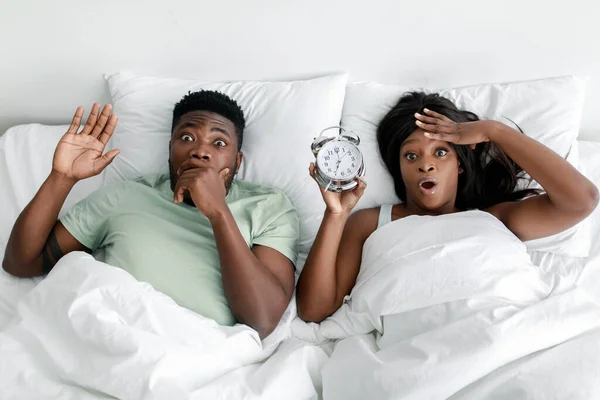 Δυσάρεστο αστείο σοκαρισμένο νεαρό Αφροαμερικάνο ζευγάρι ξυπνάει από το ξυπνητήρι. — Φωτογραφία Αρχείου