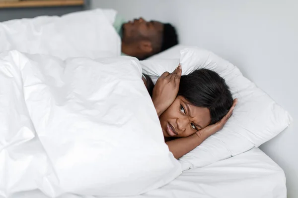 우울 한 젊은 아프리카 계 미국인 여자가 코고는 소리와 잠 자는 남편의 소음때문에 깨어나다 — 스톡 사진