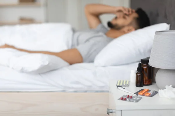 Beteg fiatal arab férfi fekszik az ágyban gyógyszerekkel az éjjeliszekrényen — Stock Fotó