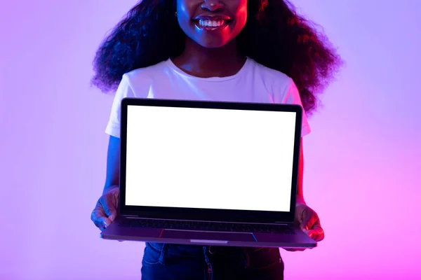 Mujer negra joven irreconocible sosteniendo ordenador portátil con pantalla vacía en luz de neón, maqueta para el diseño del sitio web — Foto de Stock
