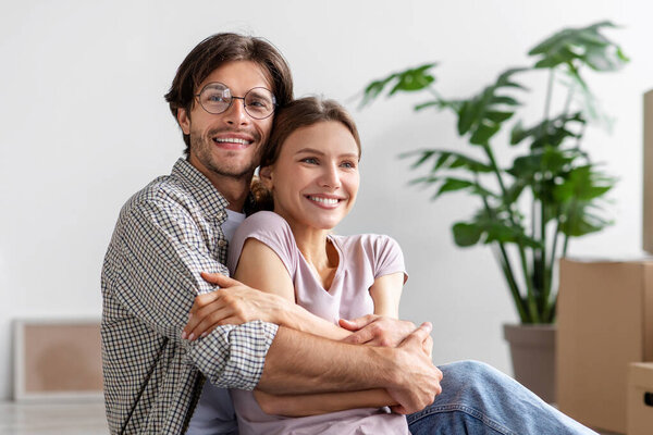 Satisfied european millennial male in glasses hugs female among cardboard boxes with stuff in room