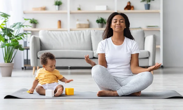 Conceito de Bem-estar Mental. Calma mãe negra feliz meditando com o bebê em casa — Fotografia de Stock