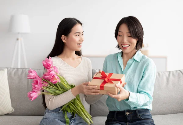 Šťastný dospělý asijské dcera dávat ji zralý maminka kytice květin a dárkové krabice, pozdrav ji s ženy den doma — Stock fotografie