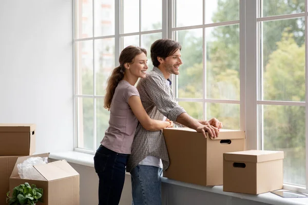 Щасливий молодий європеєць і жінка з картонними коробками виглядають у своїй квартирі вікно панорами. — стокове фото