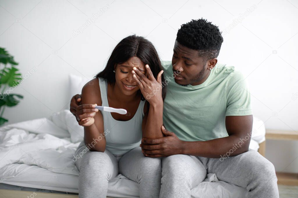 Despaired sad young african american husband hug, calm and supporting depressed wife, holding pregnancy test