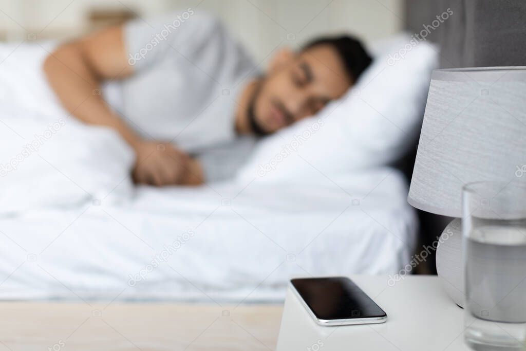 Arab Man Sleeping In Bed With Blank Smartphone Lying On Bedside Table