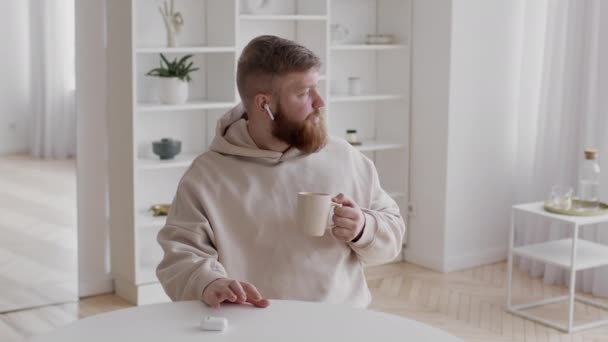 Tipo barbudo escuchando música usando auriculares inalámbricos en casa — Vídeos de Stock