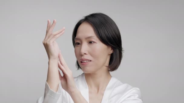 Зріла корейська жінка торкається рук шкіряного пневмонії, сірого тла — стокове відео