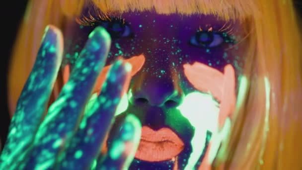 Extrem närbild av ung kvinna med ljusa neon makeup smeta glödande fluorescerande färg på hennes ansikte — Stockvideo