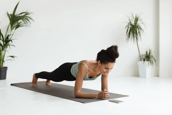 Mujer joven haciendo entrenamiento de fitness en casa, viendo videos tutoriales en Smartphone —  Fotos de Stock