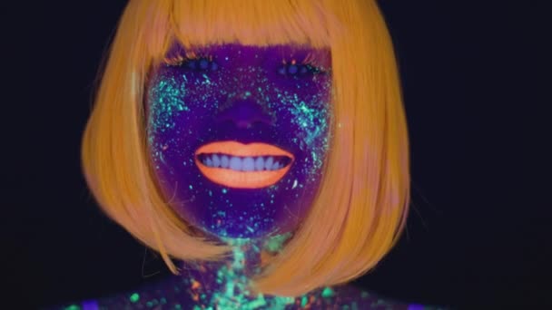 Neon schoonheid. close-up portret van jonge mooie dame met heldere gloeiende fluorescerende make-up glimlachen naar camera — Stockvideo
