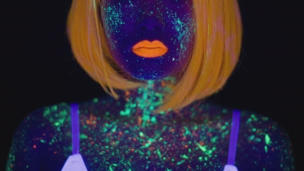 Neon body art. Tracking shot portret van jonge aziatische vrouw met gloeiende verf op borst en gezicht op zoek naar camera — Stockvideo