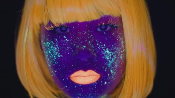 Крупним планом портрет молодої азіатки з ультрафіолетовим космічним макіяжем і помаранчевою перукою і губами, дивлячись на камеру — стокове відео