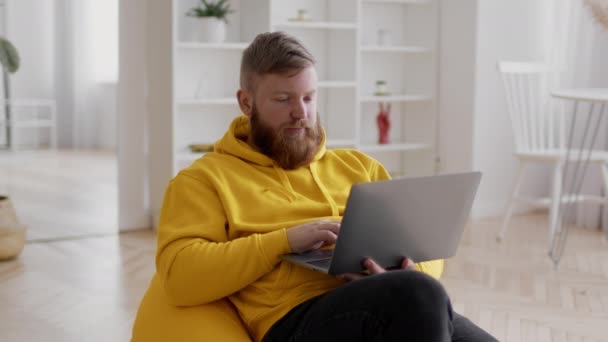 Freelancer cara usando laptop trabalhando on-line na cadeira Beanbag interior — Vídeo de Stock
