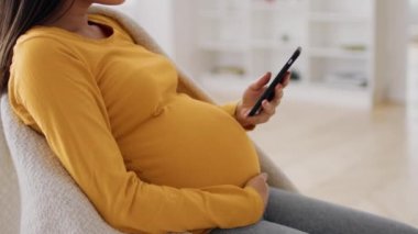 Hamilelik Uygulaması. Genç hamile kadın akıllı telefonuyla evde dinleniyor.