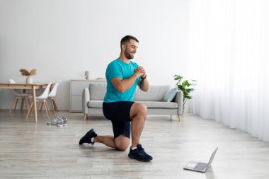 Gülümseyen genç kaslı beyaz adam bacak egzersizleri yapıyor ve online bilgisayar dersi izliyor.