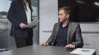 Başkanlık koltuğunda oturan genç adam, tanınmayan kadın sekreter imza için belge getiriyor, patron kontrat imzalıyor.
