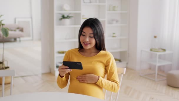 Jóvenes embarazadas mujer asiática viendo vídeos en el teléfono inteligente mientras se relaja en casa — Vídeos de Stock