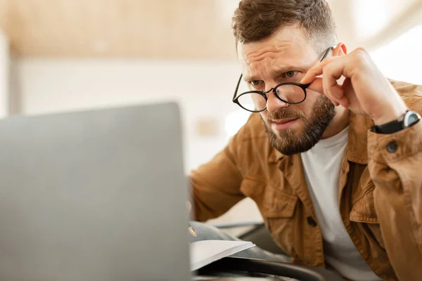 Empresário chocado olhando para o laptop acima dos óculos com problema no interior — Fotografia de Stock