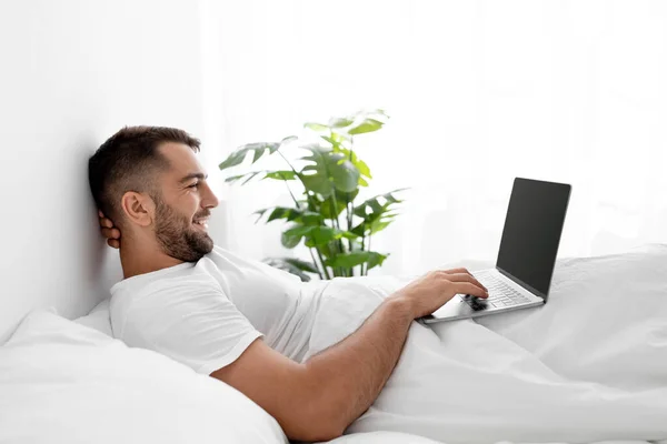 Feliz caucásico atractivo millennial masculino en camiseta blanca despertó, surfing, búsquedas y chat y trabajo en PC — Foto de Stock