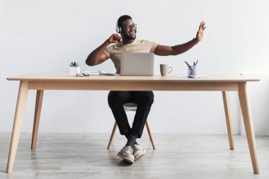 Kulaklıklı neşeli genç siyahi adam. Bilgisayarda müşteriyle sohbet ediyor. Modern ofiste masa başında oturuyor.