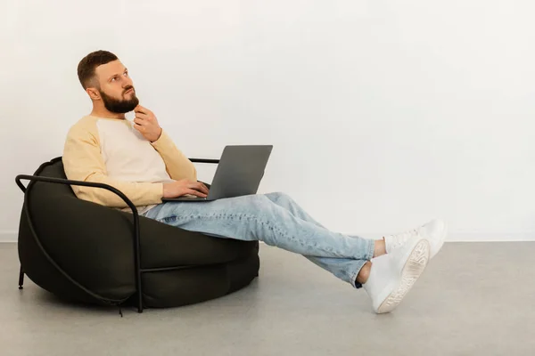 Uomo premuroso che utilizza il computer portatile che pensa seduto in sedia a casa — Foto Stock