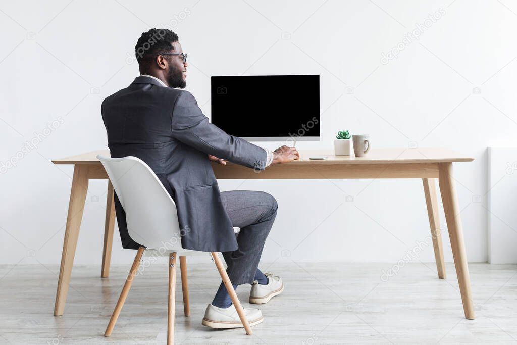 Black businessman in formal suit sitting at table, working with computer, mockup for website design