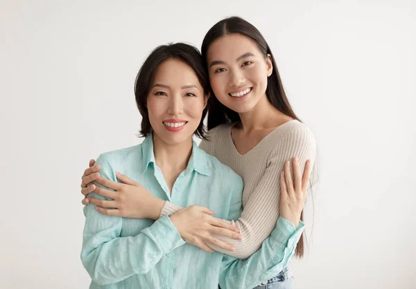Joyeuse jeune femme asiatique et sa mère aînée étreignant et souriant à la caméra sur fond de studio blanc — Photo