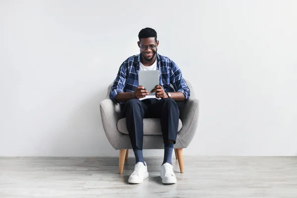 Volledige lengte van Happy jonge zwarte man met tablet zitten in fauteuil, werken of studeren online, met video chat — Stockfoto