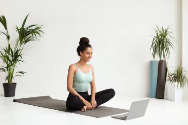 Spor yapan genç bir kadın laptopta online antrenman izlerken yoga yapıyor.