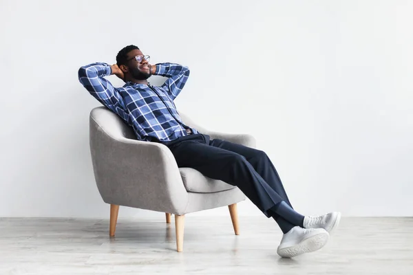 Tranquilo joven negro hombre relajante en sillón contra la pared del estudio blanco, espacio libre — Foto de Stock