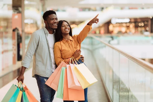 Retrato de pareja negra con bolsas de compras apuntando a la ventana —  Fotos de Stock
