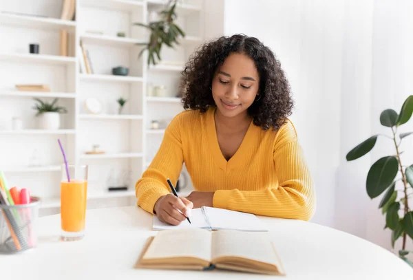 Joven mujer negra escribiendo en el cuaderno, preparándose para el examen o prueba, sentado en el escritorio en el interior —  Fotos de Stock