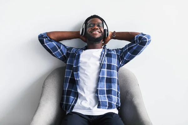 Χαλαρός Αφροαμερικανός που ακούει μουσική με ασύρματα ακουστικά, ξαπλωμένος στην πολυθρόνα με τα χέρια πίσω από το κεφάλι — Φωτογραφία Αρχείου