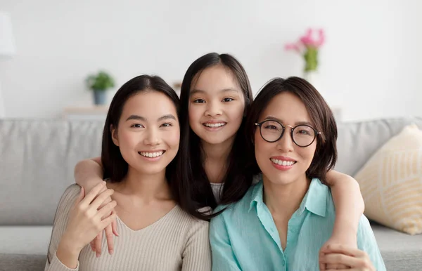 Retrato de alegre família asiática de mãe madura, filha adulta e neta sorrindo para a câmera em casa — Fotografia de Stock
