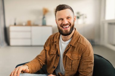 Mutlu sakallı adam gülümseyerek evde oturuyor.