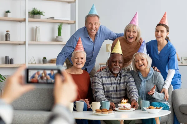 Позитивные пожилые люди и медсестра празднуют день рождения, фотографируют — стоковое фото
