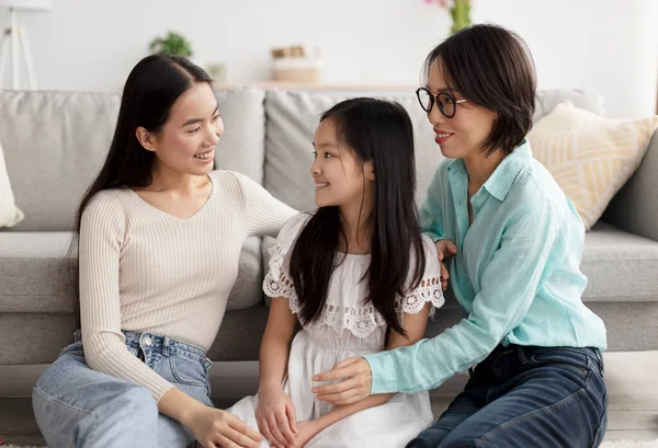Linda niña asiática con su mamá y su abuela mirándose, sentadas en el suelo en la sala de estar — Foto de Stock