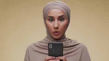 Harika bir teklif ve tanıtım. Heyecanlı tesettürlü genç Müslüman kadın cep telefonundan kazanan mesajı okuyor ve kameraya gülümsüyor.