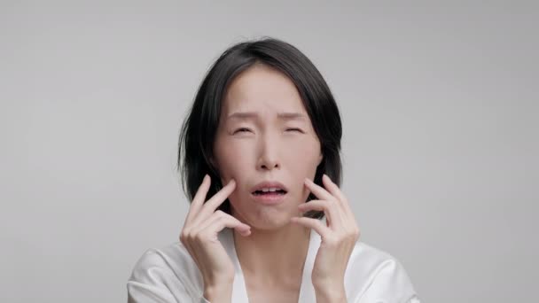 Корейська доросла жінка торкається масажу обличчя, сіре тло — стокове відео