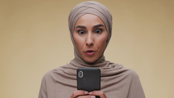 Gran oferta y promoción. Joven mujer musulmana emocionada en hijab leyendo el mensaje ganador en el teléfono celular y sonriendo a la cámara — Vídeo de stock