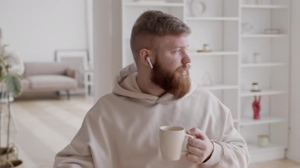 Bärtiger Mann mit Ohrhörern hört zu Hause Musik und genießt Kaffee — Stockvideo