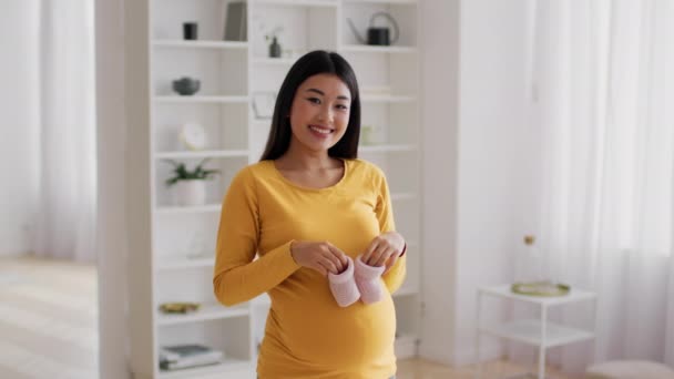 Güzel, genç, hamile, Asyalı bir kadın karnında küçük pembe bebek ayakkabıları tutuyor. — Stok video