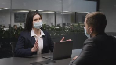 Yeni normal ve iş görüşmeleri. Koruyucu maskeli genç iş kadını ofiste erkek ortağıyla konuşuyor.