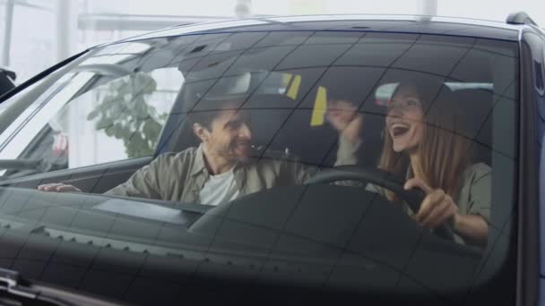 Glada bilägare. Ung upphetsad man och kvinna dansar i ny bil, njuter av inköp av ny bil på showroom — Stockvideo