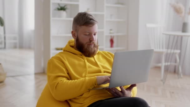 Barbudo hombre usando ordenador portátil de trabajo en línea sentado en casa — Vídeo de stock