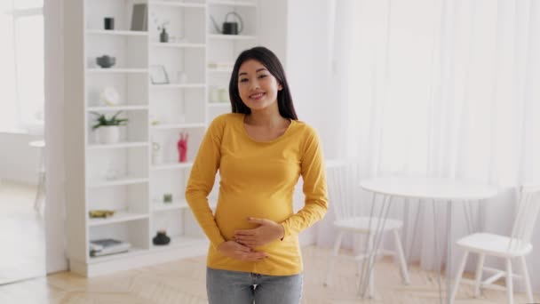 Gelukkige verwachting. Portret van jonge zwangere aziatische dame poseren in huis interieur — Stockvideo