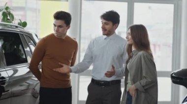 Profesyonel satış temsilcisi araba galerisindeki birkaç müşteriye danışıyor, araçların faydalarını anlatıyor, çekim takibini yapıyor.